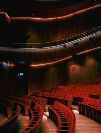 A beautifully lit theater with curved rows of red seats and wood paneling.
